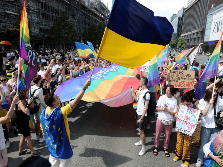 Demonstrierende halten Regenbogenfahren und einePerson schwenkt Fahne der Ukraine